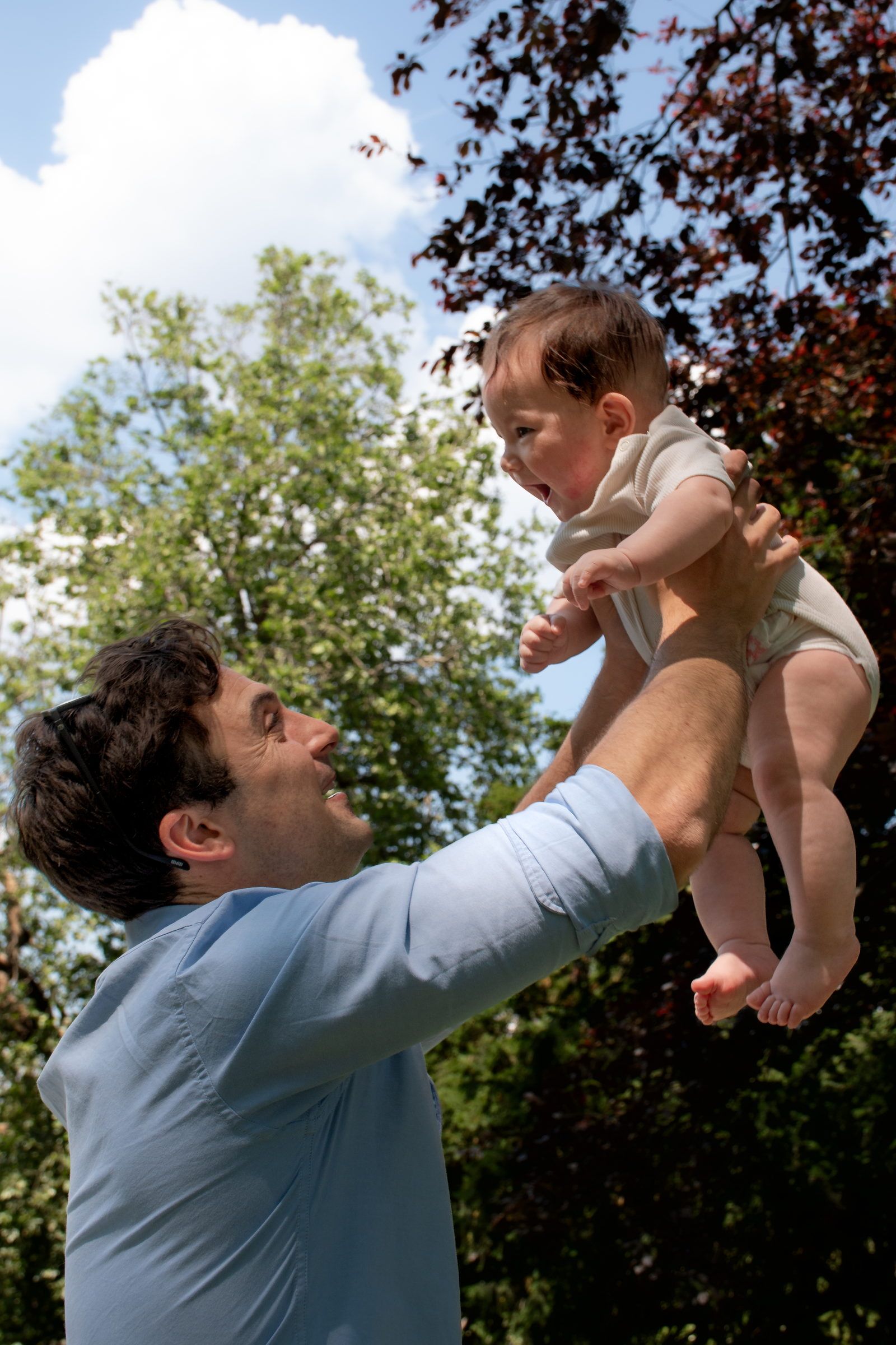 Un papa soulève son bébé vers le ciel, tous les deux rient