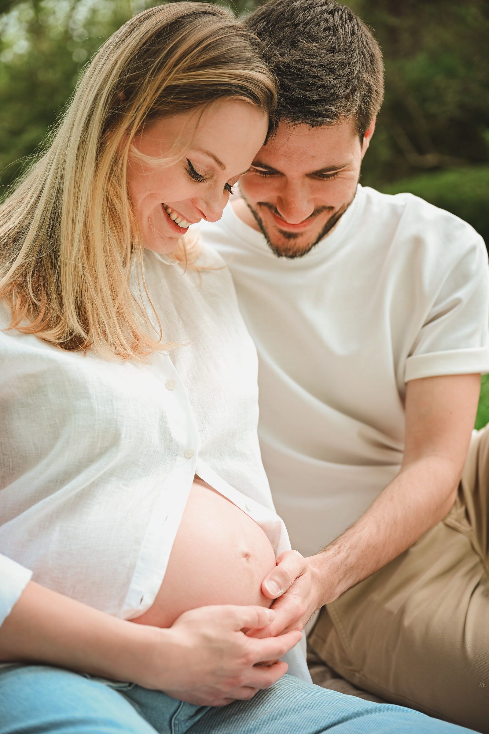 Futurs parents tête contre tête, qui regardent le ventre en souriant