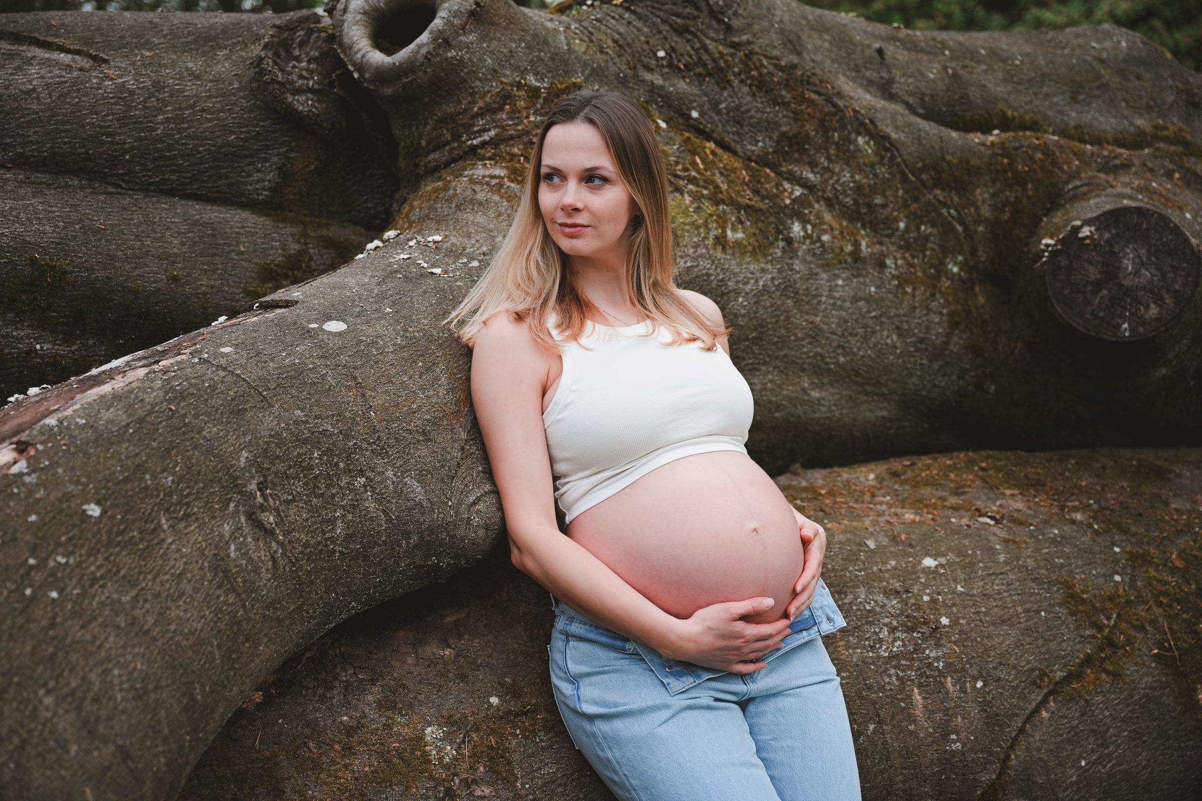 Femme enceinte adossée aux racines d’un grand arbre, plan large