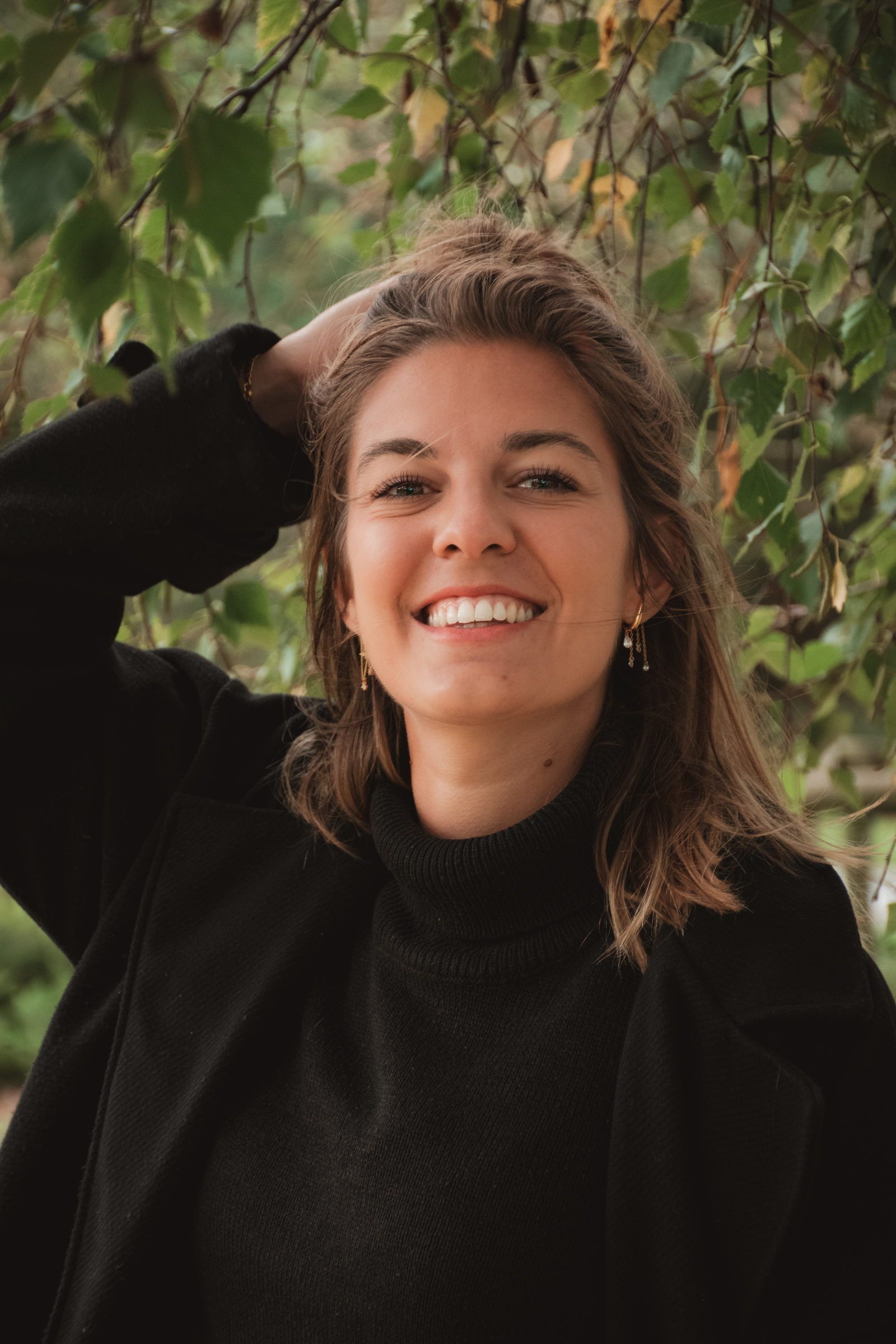 Femme qui rit, la main dans les cheveux, sous un feuillage d’automne