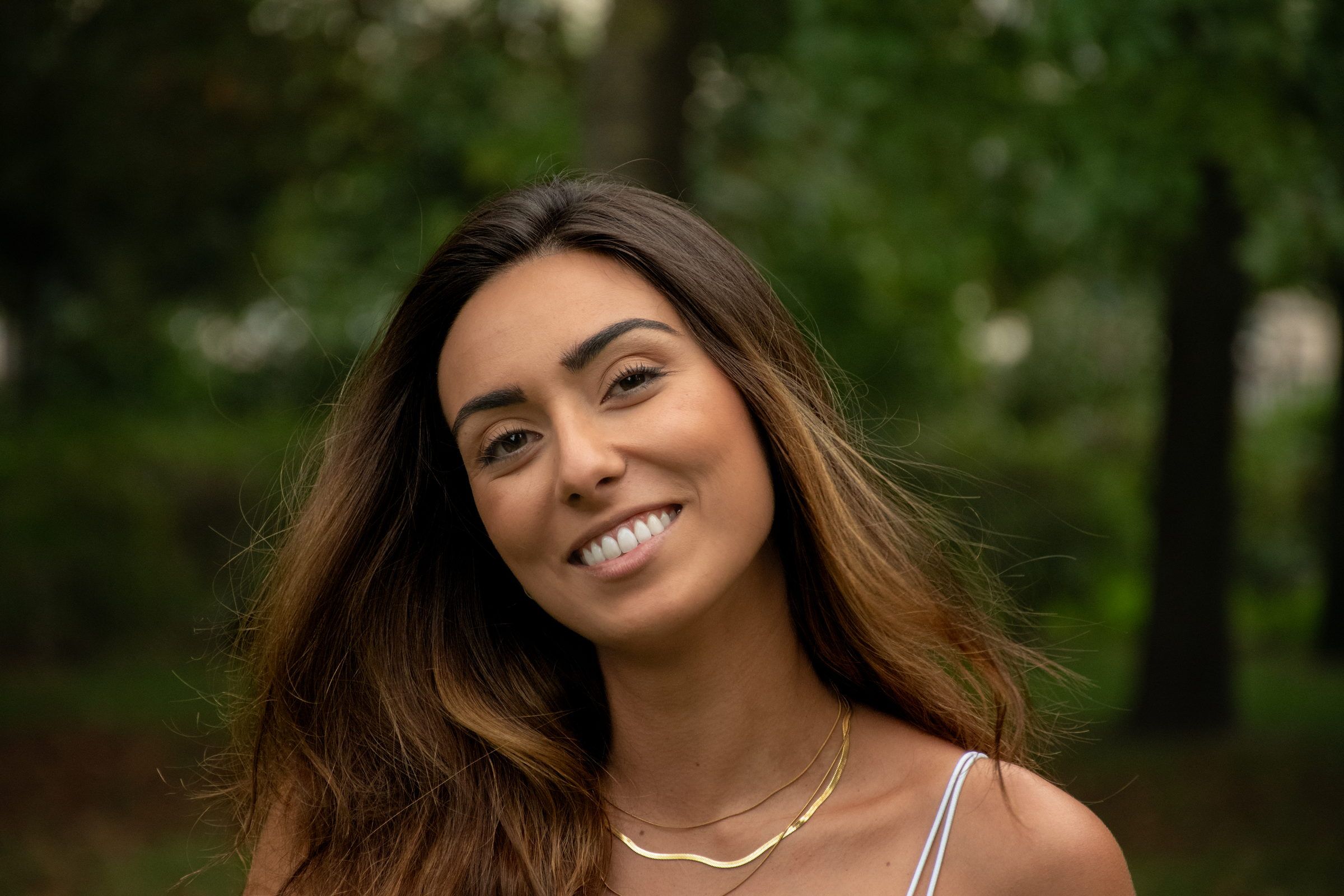 Femme souriante dans un parc, la tête penchée, lumière douce