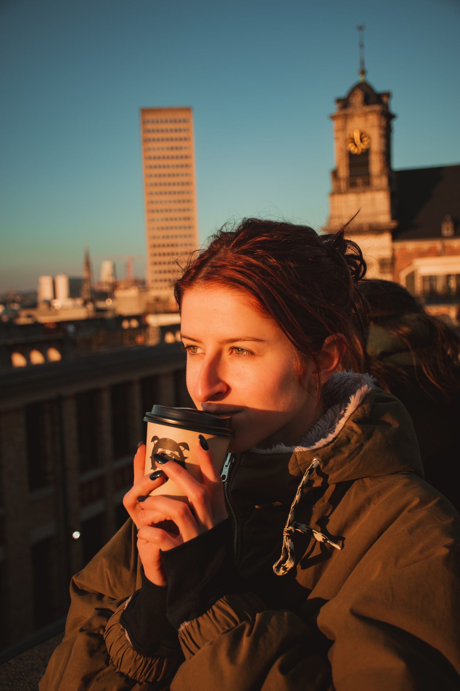 Femme qui boit un café sur les toits de Bruxelles au coucher du soleil
